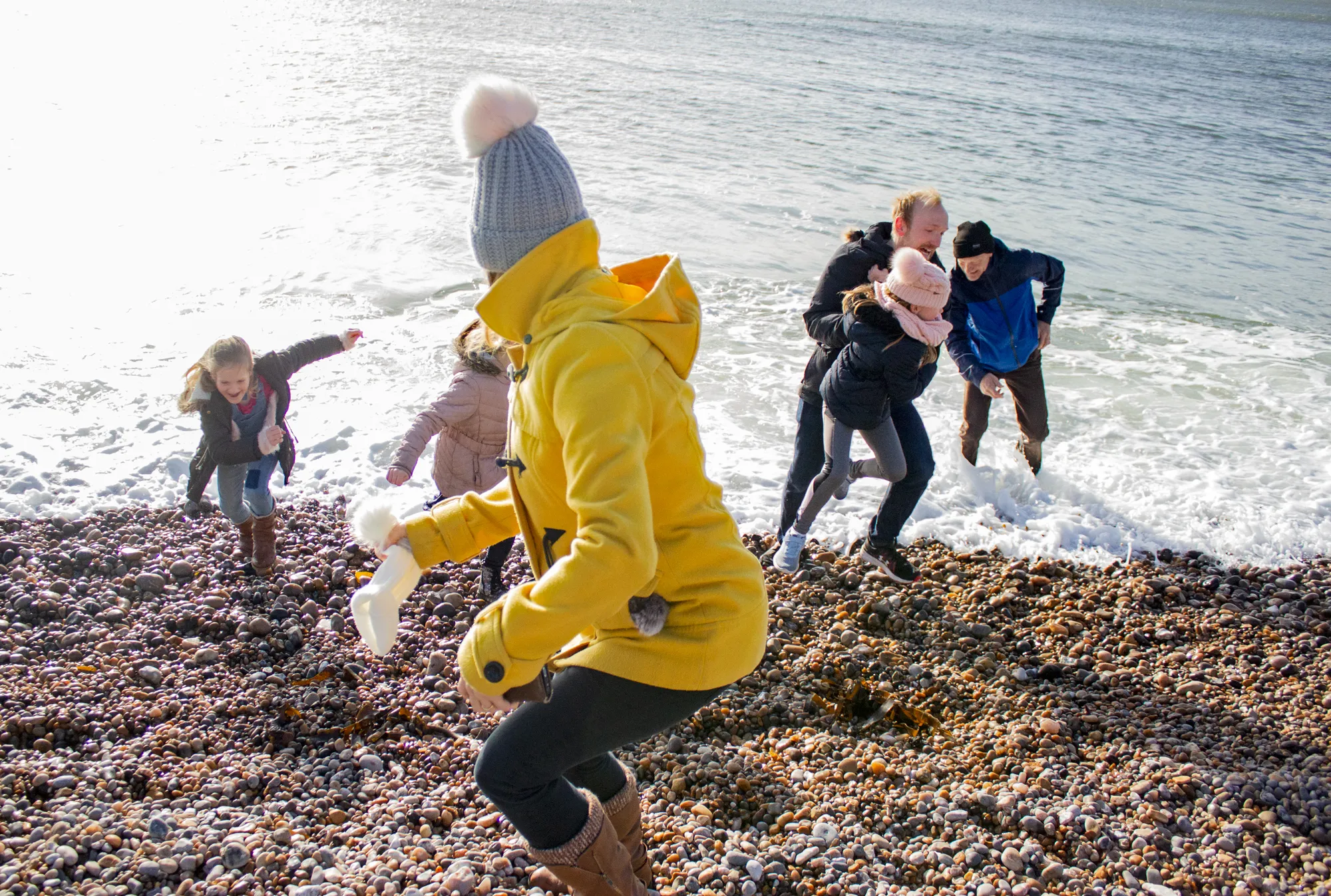 A group running up a beach chased by a wave.