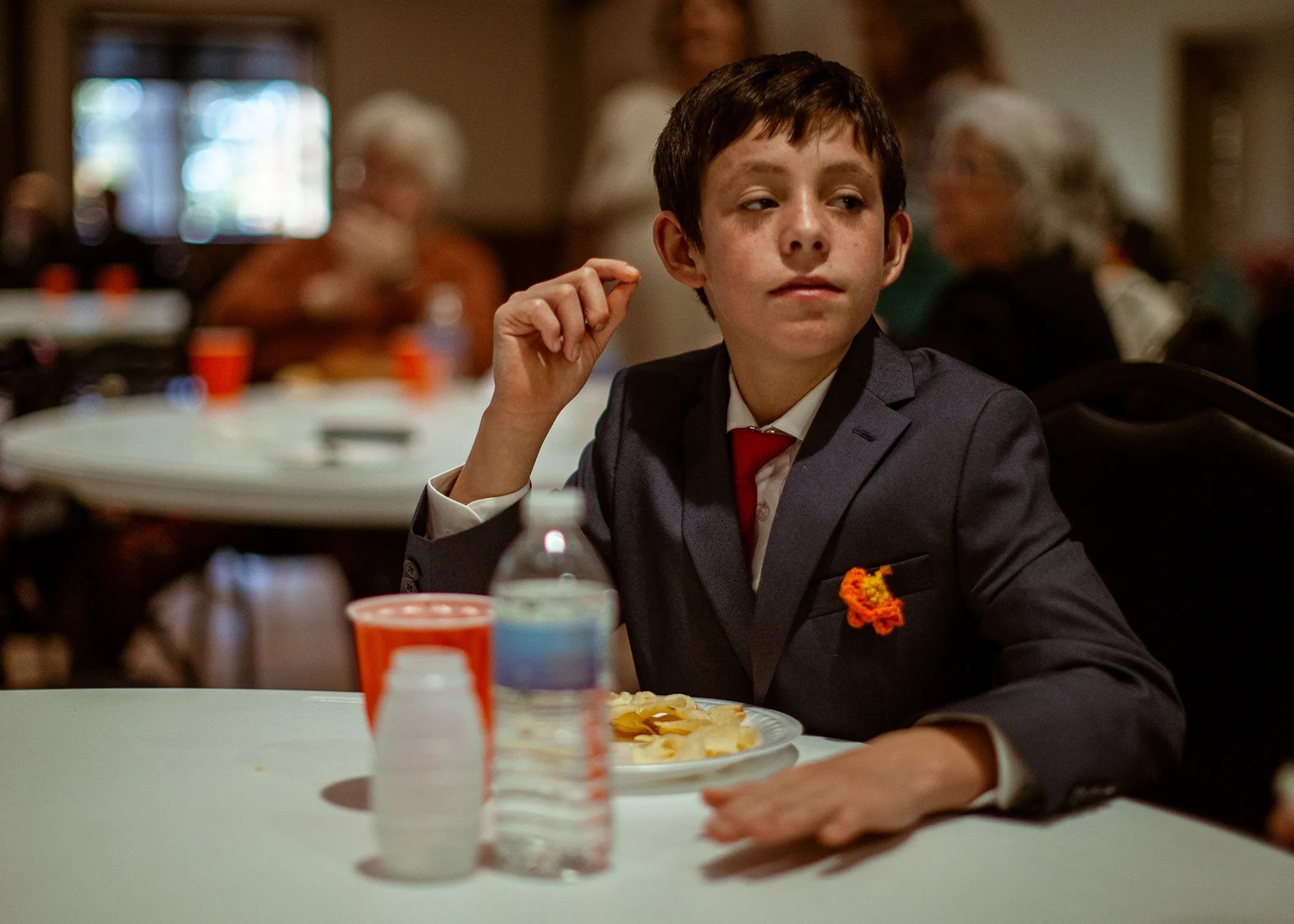 A young boy in a suit sits at a table.