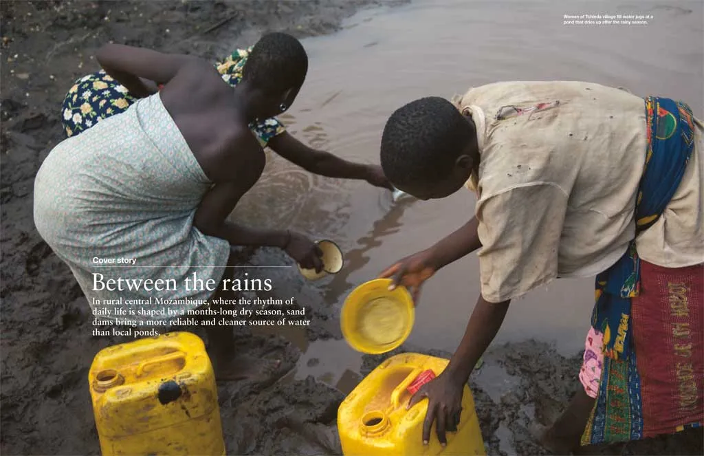A group of women bend to fill containers at edge of a watering hole